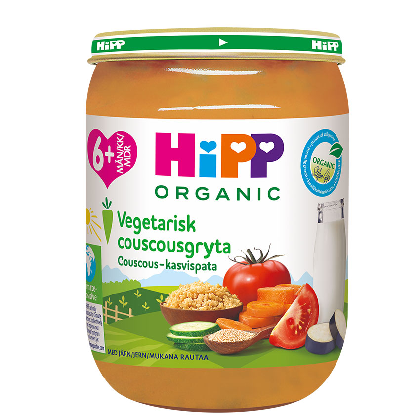 Vihreällä kannella varustettu läpinäkyvä purkki, jossa lukee "HiPP ORGANIC Vegetarisk couscousgryta Couscous-kasvispata", sisältää sekoituksen couscousia, viipaloituja tomaatteja, kurkkuja, porkkanoita ja lasillisen maitoa.